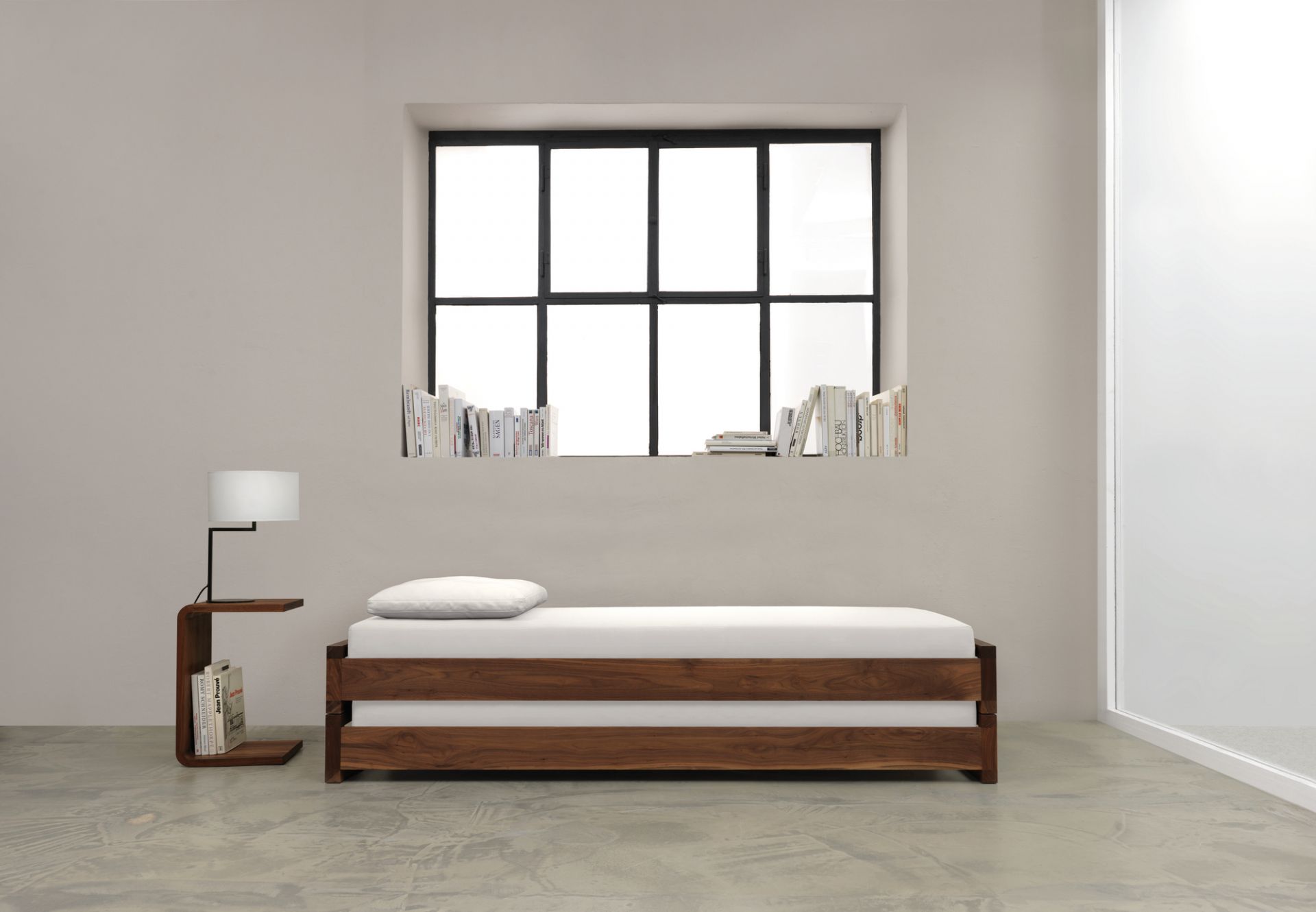 Waitress Beistelltisch aus Nussbaumholz neben einem minimalistischen Bett mit weißer Matratze und Lampe.